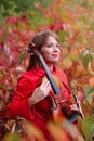 Young beautiful woman holding violin among fall colored red and green leaves in autumn Royalty Free Stock Photo