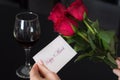 Girl holds a paper card with a message Happy 8. March in her hand and red rose and wine glass on black table Royalty Free Stock Photo