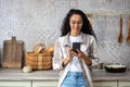 A young beautiful woman at home in kitchen smiles contentedly, browses social networks, online Internet pages, holds Royalty Free Stock Photo