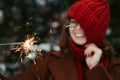 Young beautiful woman in knitted red hat and scarf standing in the park with bengal light, sparkler. Concept celebration Royalty Free Stock Photo