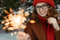 Young beautiful woman in knitted red hat and scarf standing in the park with bengal light, sparkler. Concept celebration Royalty Free Stock Photo