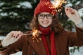 Young beautiful woman in knitted red hat and scarf standing in the park with bengal light, sparkler. Concept celebration Royalty Free Stock Photo