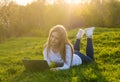 Young beautiful woman with a laptop lies on the grass in sunset Royalty Free Stock Photo