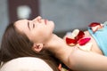 Young beautiful woman laying and relaxing in spa after massage with rose flower petals. Royalty Free Stock Photo