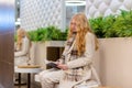 Young beautiful woman in light coat sitting on the bench inside a shoping mall and reading book Royalty Free Stock Photo