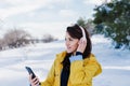 young beautiful woman listening to music on mobile phone and headset in the snow. wearing yellow coat, winter lifestyle Royalty Free Stock Photo