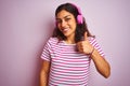 Young beautiful woman listening to music using headphones over isolated pink background doing happy thumbs up gesture with hand Royalty Free Stock Photo