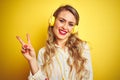 Young beautiful woman listening to music using headphones over yellow isolated background smiling with happy face winking at the Royalty Free Stock Photo