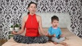 Young beautiful woman with little son meditating on bed at home. Morning fitness Royalty Free Stock Photo