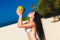 Young beautiful woman with long black hair in white bikini, drinking coconut water on tropical beach Royalty Free Stock Photo