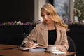 Young beautiful woman with long blonde hair drinking coffee and writing diary, book or notes in a street cafe Royalty Free Stock Photo