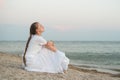Young beautiful woman with long braid sits by the sea and dreams Royalty Free Stock Photo