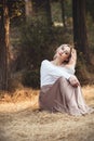 Young beautiful woman in a long dress on a background of dry grass sitting on glade in the forest, romantic girl relaxing alone in Royalty Free Stock Photo