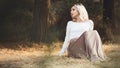 Young beautiful woman in a long dress on a background of dry grass sitting on glade in the forest, romantic girl relaxing alone in Royalty Free Stock Photo