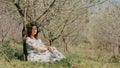 Young beautiful woman in long dress sitting under blooming plum tree Royalty Free Stock Photo