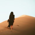 Young beautiful woman in long dress walks along sand dunes reaching top alone Royalty Free Stock Photo