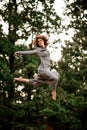 Young beautiful woman in long gray shirt magnificently jumps high in the air