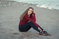 Young beautiful woman with long hair, in black jeans and red shirt, sitting on sand on beach among seagulls birds Royalty Free Stock Photo