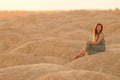 Young beautiful woman with long hair in blue dress sitting elegant on sand at sunrise in sandy desert. Looking behind Royalty Free Stock Photo