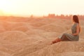 Young beautiful woman with long hair in blue dress sitting elegant and thoughtful on sand at sunrise in sandy desert Royalty Free Stock Photo