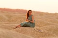 Young beautiful woman with long hair in blue dress sitting elegant and thoughtful on sand at sunrise in sandy desert Royalty Free Stock Photo