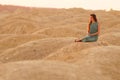 Young beautiful woman with long hair in blue dress sitting elegant and thoughtful on sand at sunrise in sandy desert Royalty Free Stock Photo