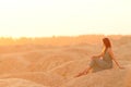 Young beautiful woman with long hair in blue dress sitting on sand at sunrise in sandy desert. Looking thoughtful down Royalty Free Stock Photo