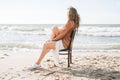 Young carefree beautiful woman with long hair in sweater sitting on chair on sea beach Royalty Free Stock Photo