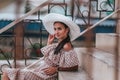 Young beautiful woman with long hair in white hat and begie dress walking in a city Royalty Free Stock Photo