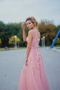 Young beautiful woman in long pink evening dress walking path in park. Fashion style portrait of gorgeous beautiful girl outdoors Royalty Free Stock Photo