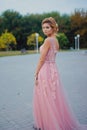 Young beautiful woman in long pink evening dress walking path in park. Fashion style portrait of gorgeous beautiful girl outdoors Royalty Free Stock Photo