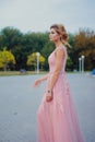 Young beautiful woman in long pink evening dress walking path in park. Fashion style portrait of gorgeous beautiful girl outdoors Royalty Free Stock Photo