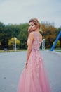 Young beautiful woman in long pink evening dress walking path in park. Fashion style portrait of gorgeous beautiful girl outdoors Royalty Free Stock Photo