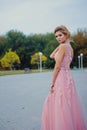 Young beautiful woman in long pink evening dress walking path in park. Fashion style portrait of gorgeous beautiful girl outdoors Royalty Free Stock Photo