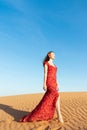 Young beautiful woman in long red dress with red rose petals among the desert. Desert rose conception. Royalty Free Stock Photo