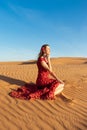 Young beautiful woman in long red dress with red rose petals among the desert. Desert rose conception. Royalty Free Stock Photo