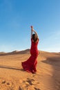 Young beautiful woman in long red dress with red rose petals among the desert. Desert rose conception. Royalty Free Stock Photo