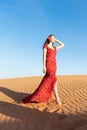 Young beautiful woman in long red dress with red rose petals among the desert. Desert rose conception. Royalty Free Stock Photo