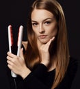 Young beautiful woman with long silky straight hair in black bodysuit holds demonstrates hair straightener over dark