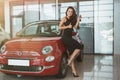 Young beautiful woman looks happy with car keys in her hand standing in dealership center near her brand new car showing Royalty Free Stock Photo