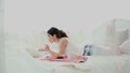 Young beautiful woman lying on the bed and using laptop. Girl surfs the Internet in morning and eating her breakfast Royalty Free Stock Photo