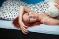 Young beautiful woman lying in bed indoors. Red hair, blue background Royalty Free Stock Photo