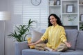 Young beautiful woman meditating at home sitting on sofa in living room in lotus pose, latin american look camera Royalty Free Stock Photo