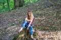 Young beautiful woman model with long hair in jeans and a tank top walks through the forest park among trees and vegetation posing Royalty Free Stock Photo