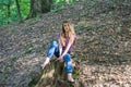 Young beautiful woman model with long hair in jeans and a tank top walks through the forest park among trees and vegetation posing Royalty Free Stock Photo