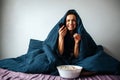 Young beautiful woman in morning bed at home. Crying under blanket. Switching tv channels with remote control. Hold Royalty Free Stock Photo