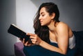 Young beautiful woman in morning bed at home. Sexy smart female person reading book at home. Leaning on her elbows and Royalty Free Stock Photo