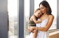 Young beautiful woman mother cuddling her baby son while standing by window at home Royalty Free Stock Photo