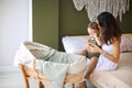 Young beautiful woman mother with sleepy baby boy son sitting on bed near bassinet Royalty Free Stock Photo