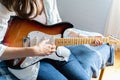 Young beautiful woman, musician, singer studying, practicing to play electric guitar at home sitting on bed in blue shirt,jeans. Royalty Free Stock Photo